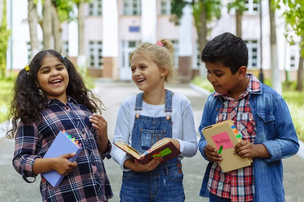 Okula dönüyoruz. Backpacks Ile üç arkadaş yakın yukarı sarılmaya ve okulun önünde gülüyor. Okul çocuklar karışık ırk grup okulda eğlenmek.