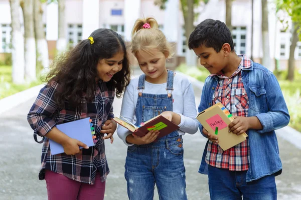 Okula dönüyoruz. Backpacks Ile üç arkadaş yakın yukarı sarılmaya ve okulun önünde gülüyor. Okul çocuklar karışık ırk grup okulda eğlenmek.