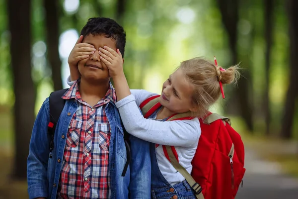 Dois amigos da escola se divertindo no parque. Garota caucasiana cobrindo os olhos para menino afro-americano surpreso . — Fotografia de Stock