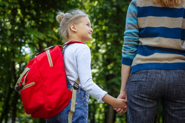 Premier jour à l'école. Femme et fille avec un sac à dos rouge derrière le dos. Début des leçons. Premier jour d'automne. Concept de retour à l'école . — Photo