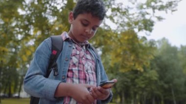 Akıllı telefon ile açık portre Afro Amerikan mutlu okul çocuk. Genç öğrenci cep telefonuna bakıyor. Okul konseptine geri dönelim. Yavaş hareket çekimi.