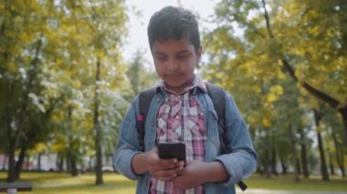 Akıllı telefon ile açık portre Afro Amerikan mutlu okul çocuk. Genç öğrenci cep telefonuna bakıyor. Okul konseptine geri dönelim. Yavaş hareket çekimi.