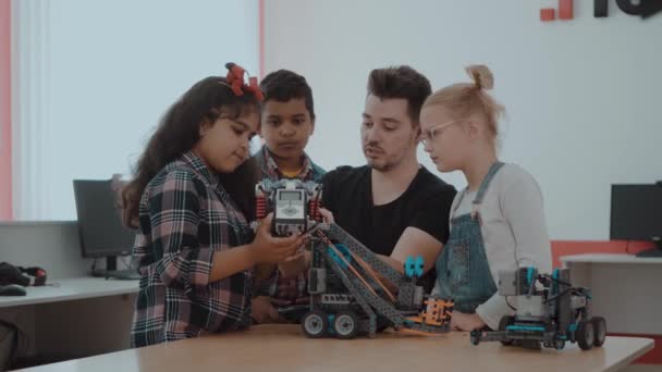 Змішана расова група дітей шкільного віку, що контролюють роботизовану машину з дистанційним керуванням разом вчителем. Творчі діти, що працюють над технічним проектом у школі . — стокове відео