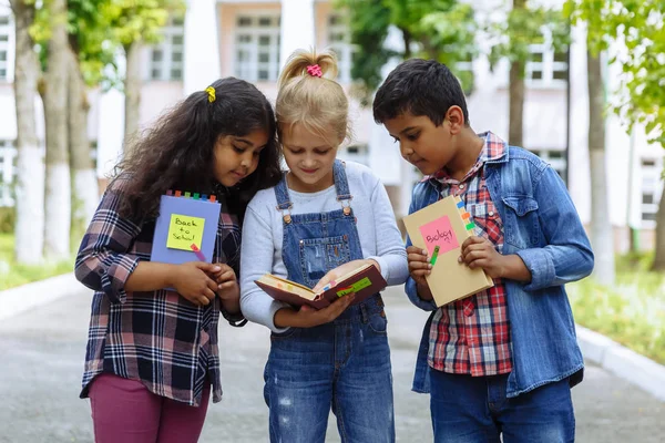 Okula dönüyoruz. Backpacks Ile üç arkadaş yakın yukarı sarılmaya ve okulun önünde gülüyor. Okul çocuklar karışık ırk grup okulda eğlenmek.