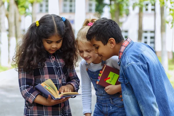 Je retourne à l'école. Fermer Trois amis avec des sacs à dos étreignant et riant devant l'école. Groupe racial mixte d'écoliers qui s'amusent dans la cour d'école . — Photo