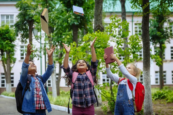 Okula dönüyoruz. Üç arkadaş backpacks Ile sarılmaya ve okulun önünde gülüyor. Okul çocuklar karışık ırksal grup okulda kitap atma eğlenceli sahip.