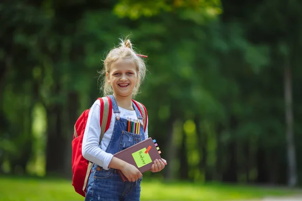 Portré boldog iskoláslány a könyv és a piros hátizsák. Vissza az iskolai koncepcióhoz. — Stock Fotó