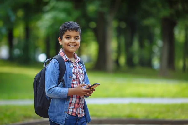 Retrato ao ar livre afro americano menino da escola feliz com smartphone. Jovem estudante olhando para o telefone celular. Voltar ao conceito de escola . — Fotografia de Stock