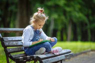 Renkli kalemler ile çizim küçük güzel okul kız, güneşli parkta bir bankta oturan