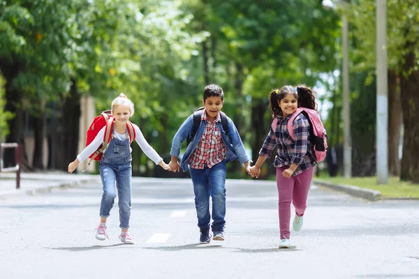 Vissza az iskolába. Vegyes faji csoport boldog általános iskolás diákok hátizsákok futó kezében a szabadban. Az alapfokú oktatás koncepciója. — Stock Fotó