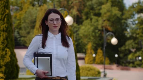 Front view of business woman with tablet pc wearing white shirt walking on a city street. Slow Motion Shot. — Stock Video