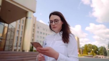 Beyaz gömlek giyen ve bir şehir caddesinde akıllı telefon kullanan iş kadını ön görünümü. Yavaş Çekim Çekimi.