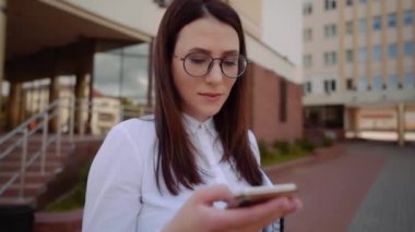 Bir şehir caddesinde akıllı telefon kullanarak beyaz gömlek giyen iş kadını ön görünümü. Yavaş Çekim Çekimi.