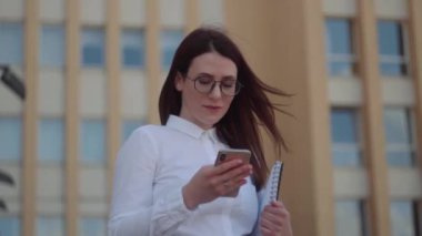 Bir şehir caddesinde akıllı telefon kullanarak beyaz gömlek giyen iş kadını ön görünümü. Yavaş Çekim Çekimi.