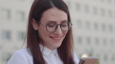 Bir şehir caddesinde akıllı telefon kullanarak beyaz gömlek giyen gülümseyen iş kadını ön görünümü. Yavaş Çekim Çekimi.