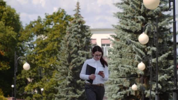 Front view of business woman wearing white shirt walking and using a smart phone on a city street. Slow Motion Shot. — Stock Video