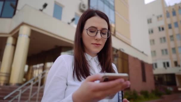 도시 거리에서 스마트 폰을 사용하여 흰색 셔츠를 입은 비즈니스 여성의 정면 전망. 슬로우 모션 샷. — 비디오