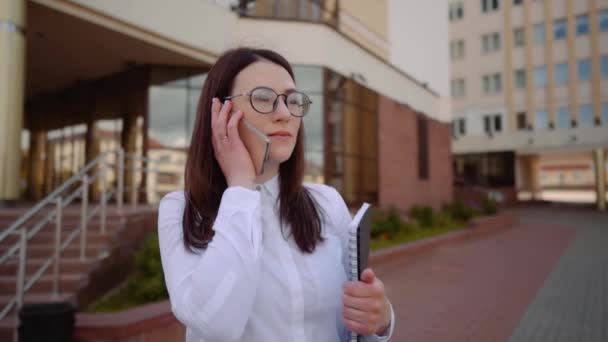 Porträt einer stilvoll lächelnden Geschäftsfrau in modischer Kleidung, die in der Nähe des Büros mit dem Handy telefoniert. Zeitlupenaufnahme. — Stockvideo