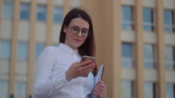 Вид спереду на ділову жінку в білій сорочці, використовуючи смартфон на міській вулиці. Повільний постріл . — стокове відео