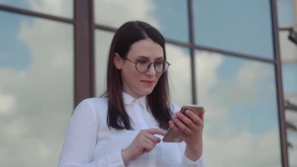 사무실 근처에서 스마트 폰 ND 문자 메시지 마사지를 사용하여 흰색 셔츠를 입은 비즈니스 여성의 초상화. 슬로우 모션 샷. — 비디오