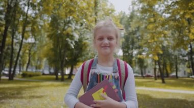 Okul bahçesinde kalan bir kitap tutan sırt çantası ile neşeli kız öğrenci. Dışarıda gülümseyen oldukça zeki bir kızın portresi. Yavaş Çekim Çekimi.