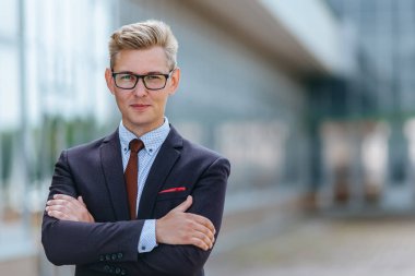 Ofis binasının önünde takım elbiseli portre adamı. Yakışıklı iş adamı dışarıda. Erkek iş adamı sokakta duruyor ve başka bir yere bakıyor. Resmi kıyafet ve gözlük giymiş işadamı.