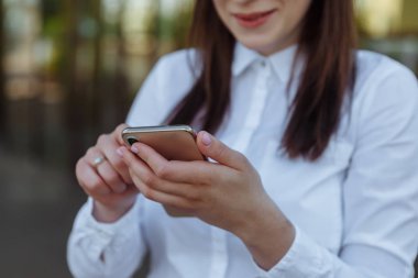 Portre genç iş kadını akıllı telefon dışarı kapı kullanarak beyaz gömlek giyiyor. Çalışma sürecinde kadın okuma sms mesajı.