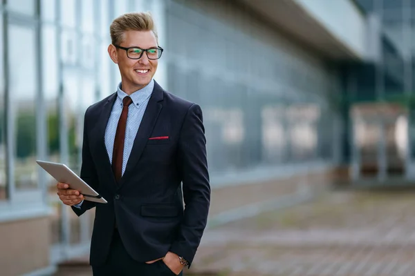 Elegant smiling young businessman using his PC tablet. Portrait of a Male executive manager in trendy clothes with tablet pc in front of office building. Modern technology concept