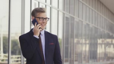 Gözlüklü genç beyaz işadamı ofis binasının önünde cep telefonuyla konuşuyor. Açık havada akıllı telefon kullanarak trendy giysiler içinde Erkek icra yöneticisi. Modern teknoloji kavramı