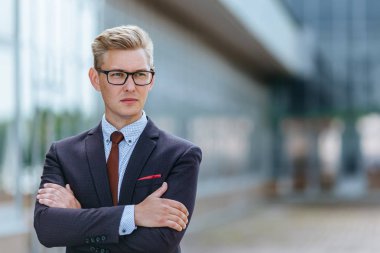 Ofis binasının önünde takım elbiseli portre adamı. Yakışıklı iş adamı dışarıda. Erkek iş adamı sokakta duruyor ve başka bir yere bakıyor. Resmi kıyafet ve gözlük giymiş işadamı.