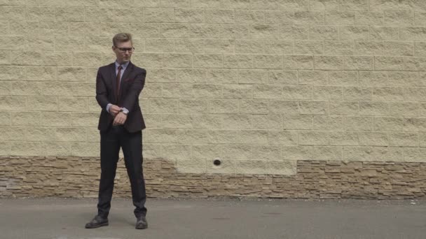 Bello e felice uomo d'affari che balla energicamente su una strada di fronte al muro di cemento urbano. Uomo sorridente che indossa un abito scuro . — Video Stock