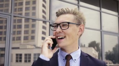 Gözlüklü genç beyaz işadamı ofis binasının önünde cep telefonuyla konuşuyor. Açık havada akıllı telefon kullanarak trendy giysiler içinde Erkek icra yöneticisi. Modern teknoloji kavramı