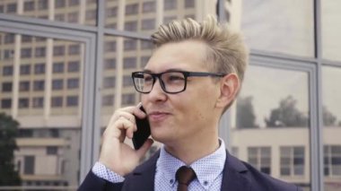 Gözlüklü genç beyaz işadamı ofis binasının önünde cep telefonuyla konuşuyor. Açık havada akıllı telefon kullanarak trendy giysiler içinde Erkek icra yöneticisi. Modern teknoloji kavramı