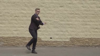 Yakışıklı ve Mutlu İşadamı Enerjik Kentsel Beton Duvar önünde bir sokakta dans. Koyu Renk Takım Elbise Giyen Gülümseyen Adam.