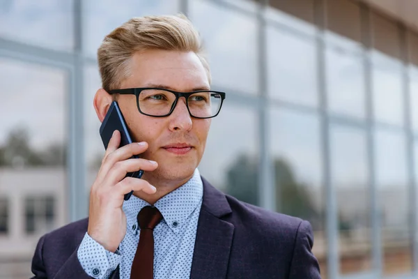 Gözlüklü genç beyaz işadamı ofis binasının önünde cep telefonuyla konuşuyor. Açık havada akıllı telefon kullanarak trendy giysiler içinde Erkek icra yöneticisi. Modern teknoloji kavramı — Stok fotoğraf