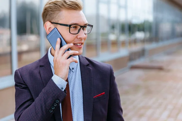 Gözlüklü genç beyaz işadamı ofis binasının önünde cep telefonuyla konuşuyor. Açık havada akıllı telefon kullanarak trendy giysiler içinde Erkek icra yöneticisi. Modern teknoloji kavramı — Stok fotoğraf