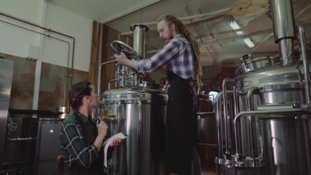 醸造所やビール工場で働くクリップボードを持つ女性。醸造所の労働者は、クラフトビール醸造所でビール樽の蓋を開けます。スモール ビジネスの概念. — ストック動画