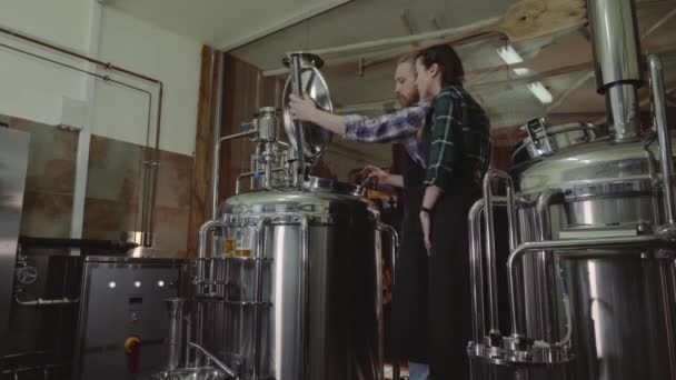 Concepto de empresa familiar. Macho y hembra trabajando con la máquina de elaboración de cerveza en una pequeña planta de cerveza . — Vídeos de Stock