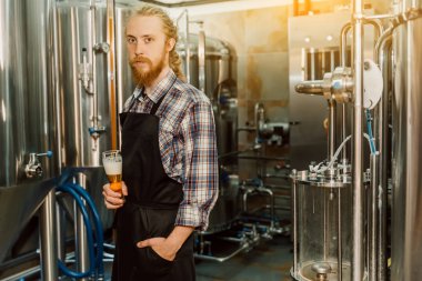 Arka planda metal kaplar ile bira üretiminde üniformalı dreadlocks ile yakışıklı bira bir portresi, kim bira evinde işyerinde bira yapıyor.