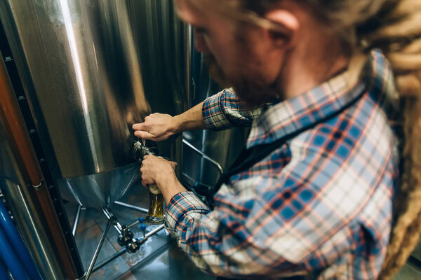 Brewer filling beer in glass from tank at brewery. Family business concept.