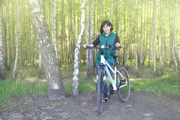 Hermosa joven. En bicicleta, de pie en el bosque contra el telón de fondo de un abedul . — Foto de Stock