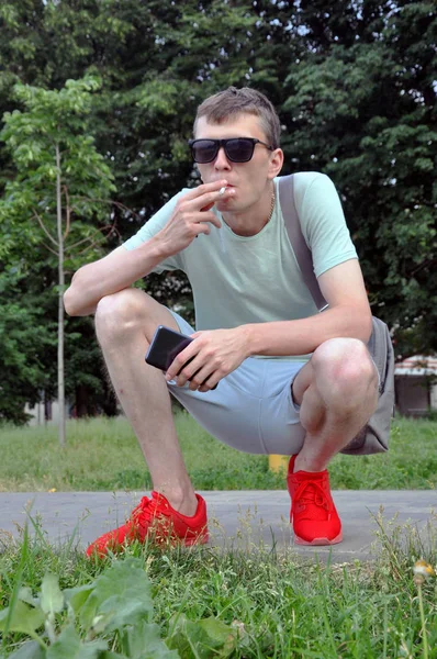 half-smoking smokes and holds the smartphone in hand