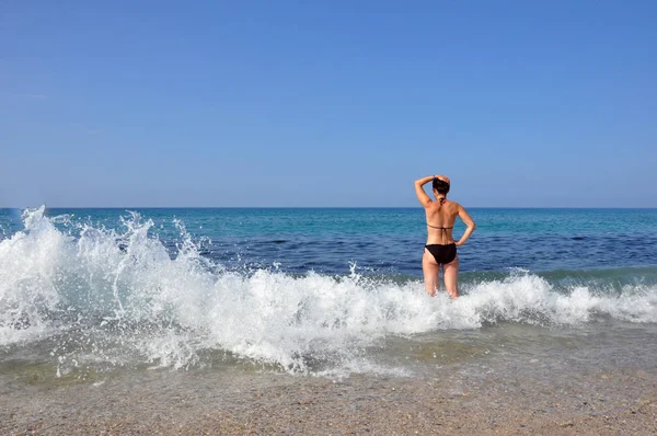 Νεαρή όμορφη γυναίκα. Μια γυναίκα με ένα μαύρο μαγιό απολαμβάνει το περπάτημα στα κύματα της θάλασσας και κάνει ηλιοθεραπεία — Φωτογραφία Αρχείου