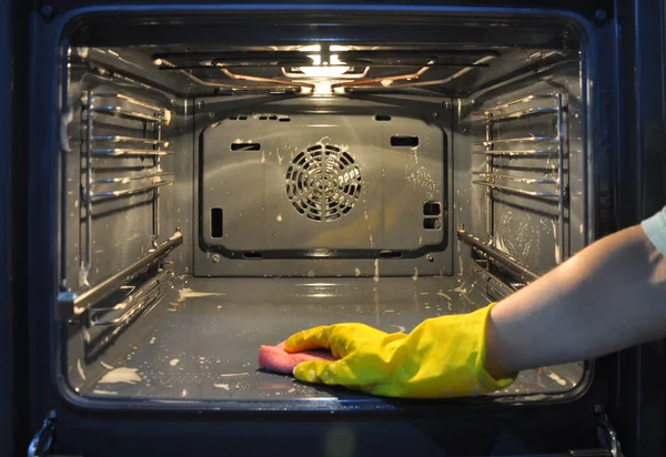 Limpieza del horno en la cocina. mano en un guante amarillo fuera de foco en el fondo del horno . — Foto de Stock