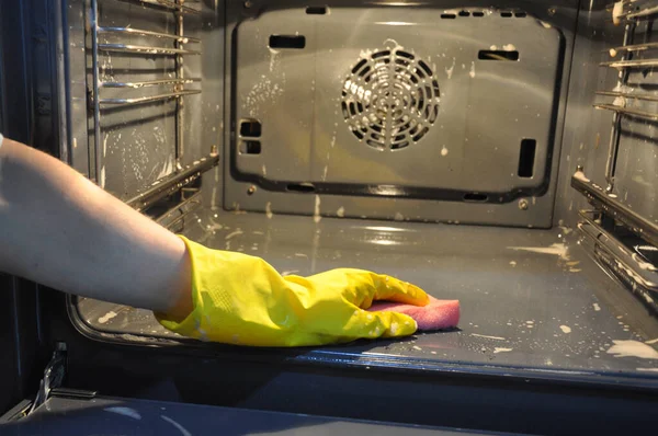 Уборка духовки на кухне. рука в желтой домашней перчатке вне фокуса на фоне печи . — стоковое фото