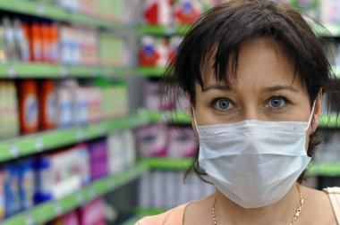 Süpermarkette tıbbi maskeli genç bir kadın kameraya bakıyor. Koronavirüs, COVID-19 ve diğer solunum enfeksiyonlarına karşı koruma kavramı.