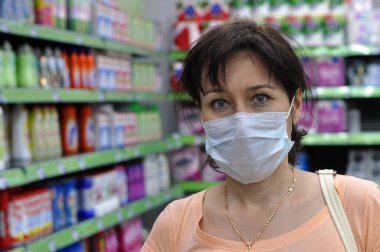 Süpermarkette tıbbi maskeli genç bir kadın kameraya bakıyor. Koronavirüs, COVID-19 ve diğer solunum enfeksiyonlarına karşı koruma kavramı.