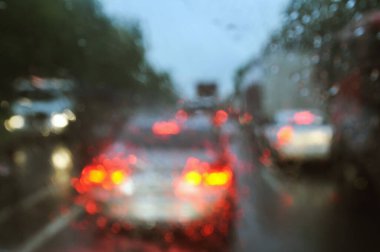 Arka planda bulanıklık, camda yağmur damlaları ve yolda arabalar. Şiddetli yağmurdan dolayı arabanın camından yol manzarası bulanıklaştı. Odak dışı, bulanık