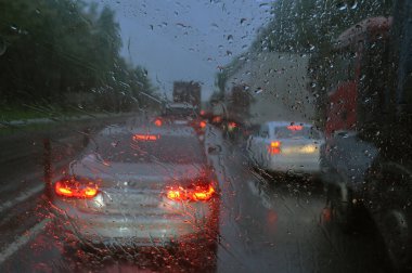 Arka planda bulanıklık, camda yağmur damlaları ve yolda arabalar. Şiddetli yağmurdan dolayı arabanın camından yol manzarası bulanıklaştı. Odak dışı, bulanık