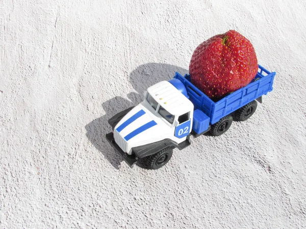 Vintage toy car with strawberries. Strawberries with toy retro car in grey concrete background. Summer vacations. Space for text. Transport logistic concept. Transportations. Vitamins and health.
